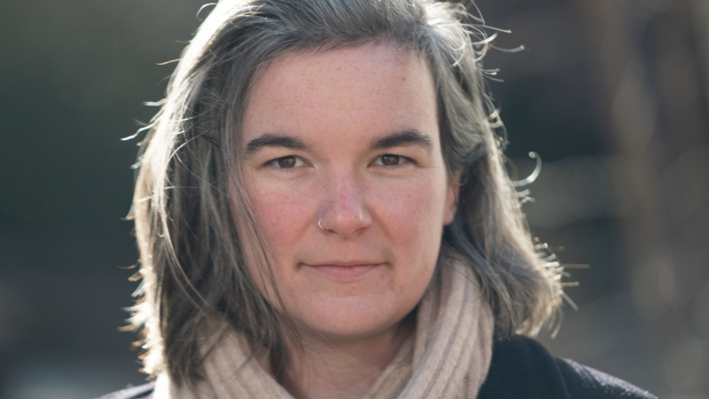 Headshot of Tiffany Fisher-Love, a woman with fair skin and gray medium length hair wearing a beige scarf